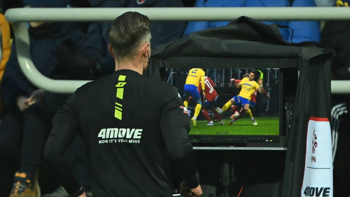 Sędzia piłkarski z numerem na plecach patrzy na ekran monitora VAR, na którym wyświetlany jest fragment gry z udziałem dwóch zawodników.