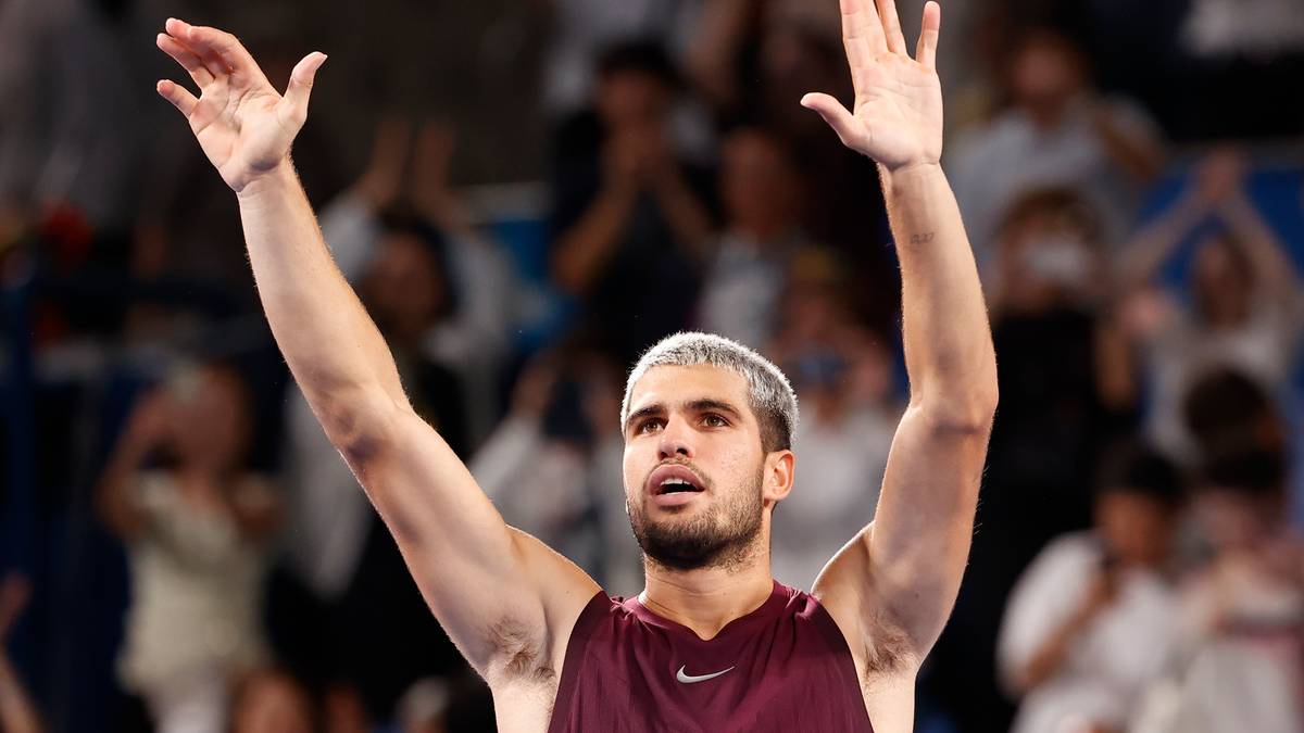 Carlos Alcaraz, tenisista, z uniesionymi rękami w geście radości, podczas meczu tenisowego.