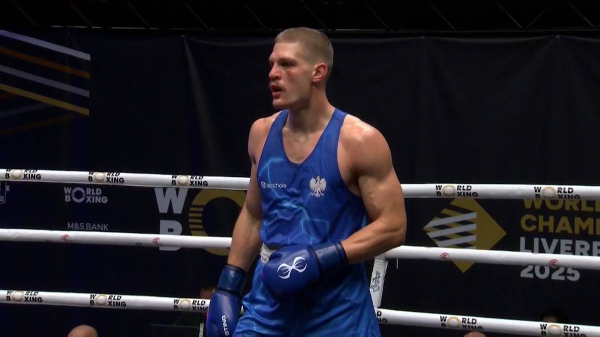 Mężczyzna w niebieskim stroju bokserskim z logo Polski na piersi stoi w ringu.