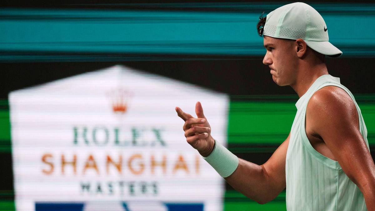 Młody mężczyzna, tenisista, w jasnym podkoszulku i czapce z daszkiem, wskazuje palcem w stronę publiczności lub kamery, z rozmytym napisem "ROLEX SHANGHAI MASTERS" w tle.
