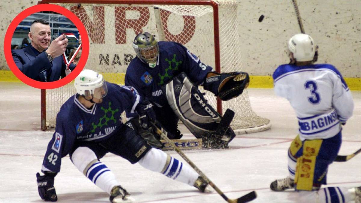 Dwóch hokeistów walczy o krążek przed bramkarzem, który jest w akcji obronnej. Jeden z zawodników stara się odebrać krążek przeciwnikowi, podczas gdy drugi jest w trakcie strzału.