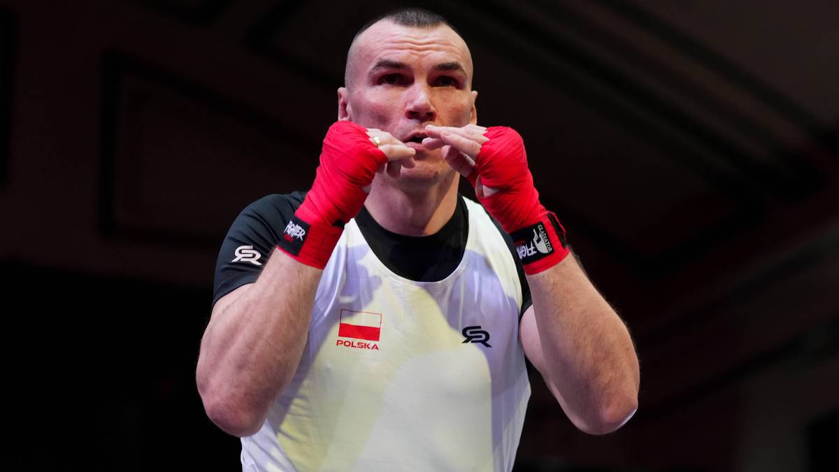 Bokser Mateusz Masternak w rękawicach bokserskich na tle ciemnego pomieszczenia