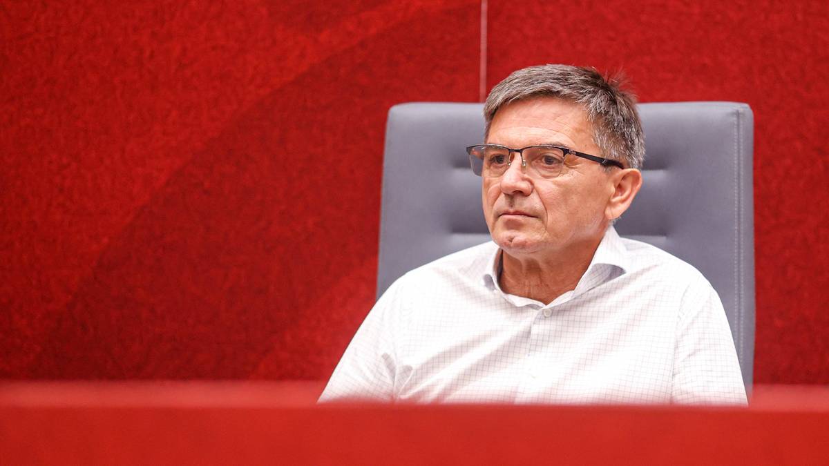 Mężczyzna w jasnej koszuli i okularach siedzi na krześle.