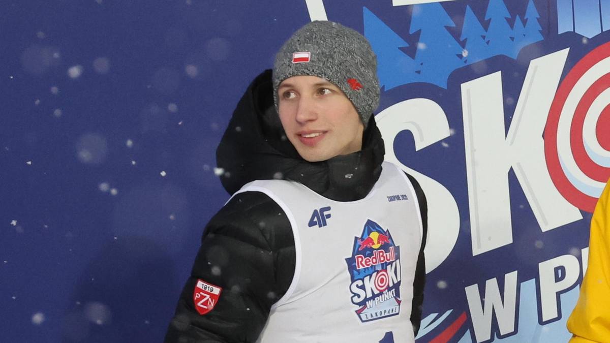 Młody skoczek narciarski Kacper Tomasiak i jego trener na tle banera Red Bull SKI JUMP.