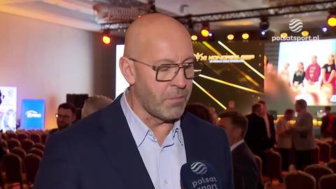 Jakub Rutnicki, ubrany w ciemną marynarkę i jasną koszulę, z okularami na nosie, wypowiada się do mikrofonu z logo "Polsat Sport". W tle widać scenę wydarzenia z podświetlanymi ekranami i publicznością siedzącą na krzesłach.