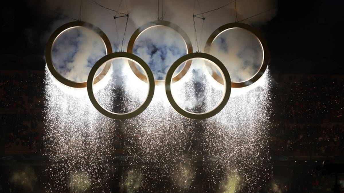 Pięć połączonych k&oacute;ł olimpijskich z efektami pirotechnicznymi w tle.