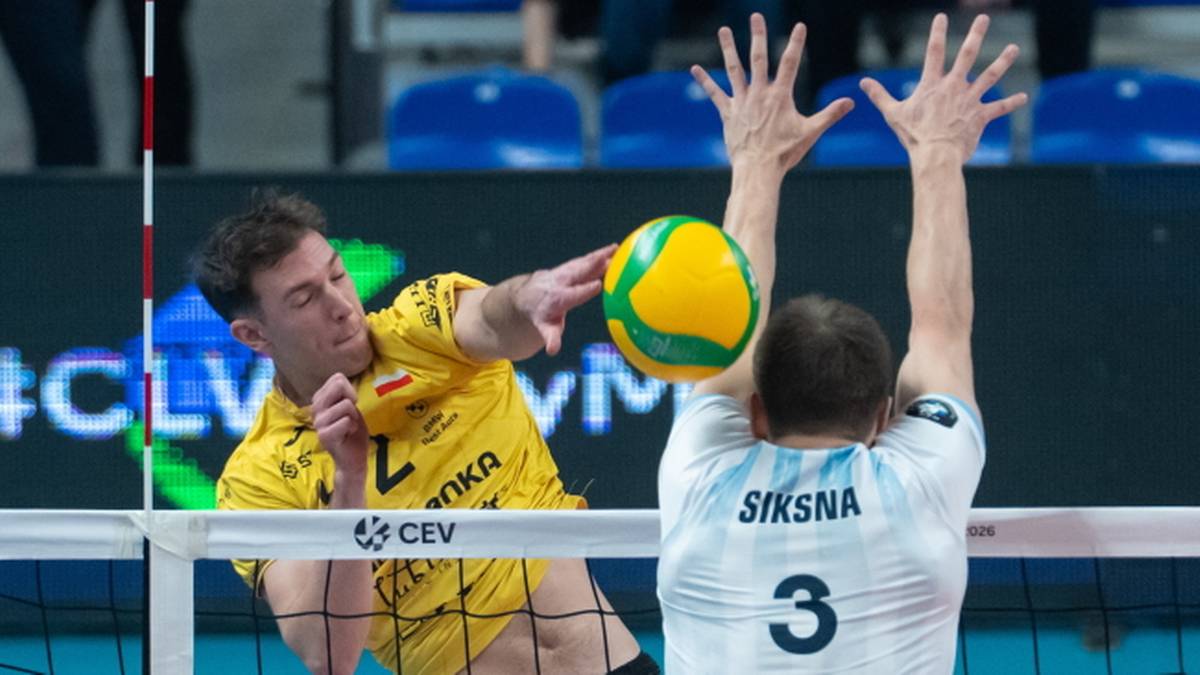 Siatkarz w ż&oacute;łtej koszulce atakuje piłkę, a siatkarz w białej koszulce blokuje.