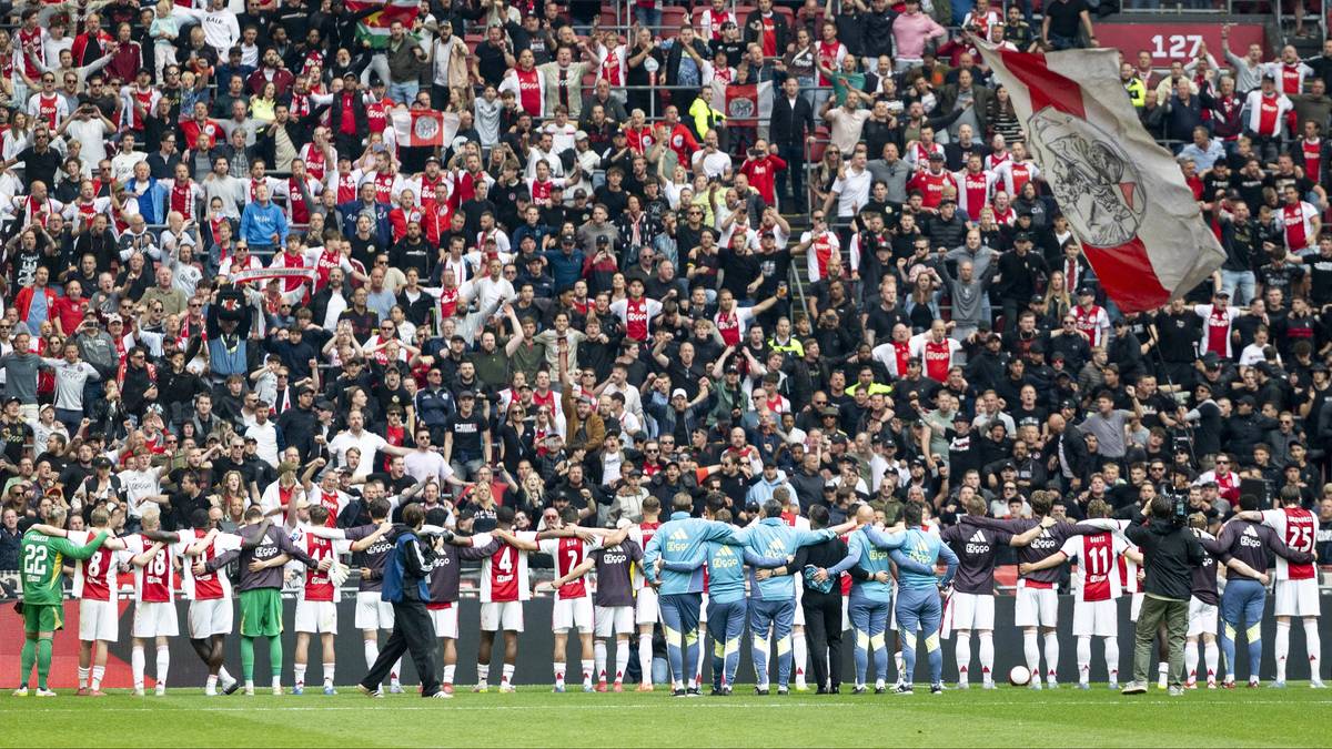 Tłum kibiców na stadionie piłkarskim, grupa piłkarzy stoi na murawie przed trybunami.
