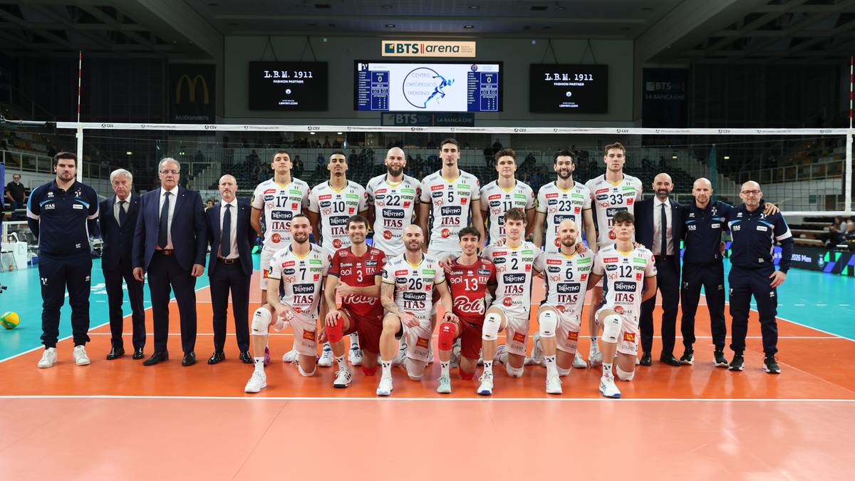 Siatkarze dw&oacute;ch drużyn w strojach sportowych pozują do zdjęcia na boisku siatkarskim.