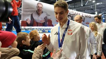 Uśmiechnięty Semirunnij w stroju sportowym z medalem na szyi, otoczony przez grupę ludzi, którym rozdaje autografy.