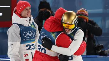 Dwie sportsmenki w strojach olimpijskich przytulają się po zawodach, wyrażając radość.