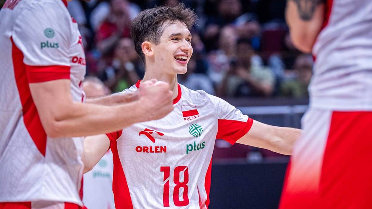Młody siatkarz w białej koszulce z numerem 18 i polskim godłem, uśmiechnięty i cieszący się z gry podczas meczu.