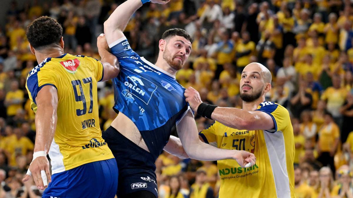 Piłkarz ręczny w niebieskiej koszulce z napisem ORLEN pr&oacute;buje rzucić piłkę do bramki, otoczony przez dw&oacute;ch przeciwnik&oacute;w w ż&oacute;łtych strojach.