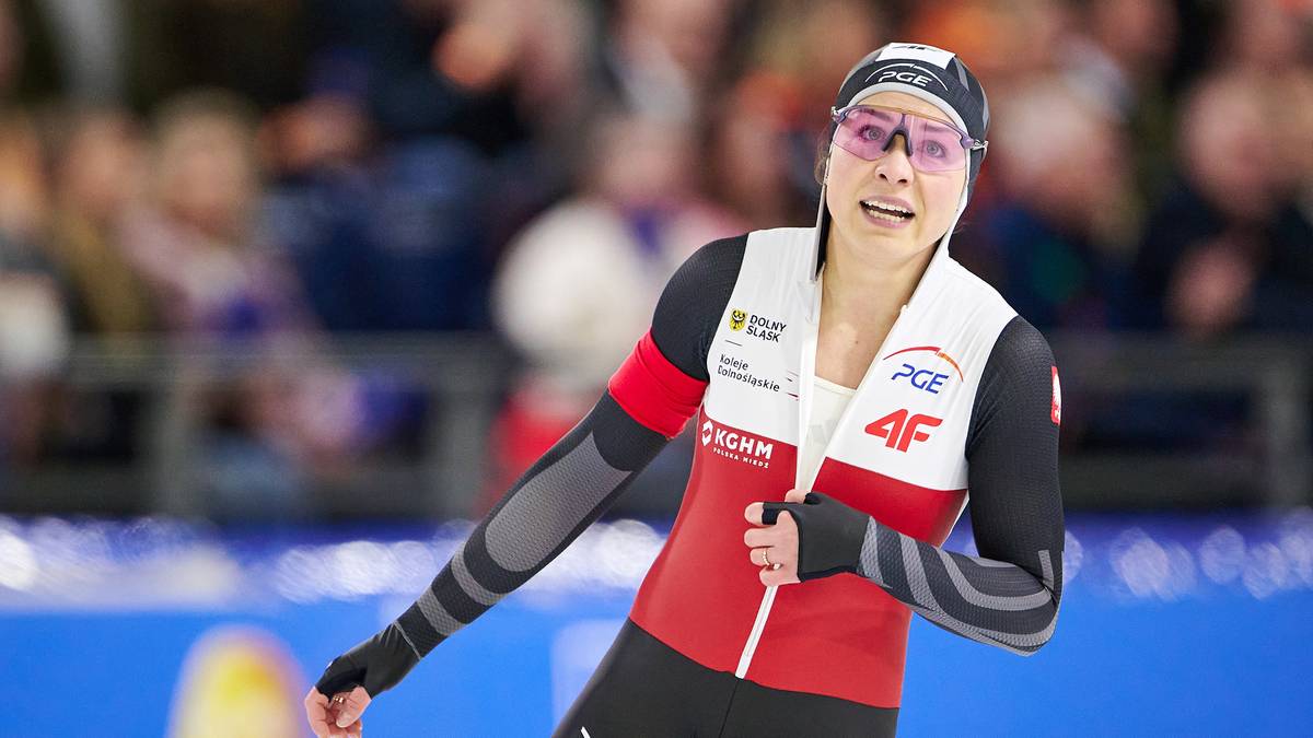 Łyżwiarka w czerwono-białym stroju sportowym, z okularami na głowie, biegnie po lodzie podczas zawod&oacute;w.