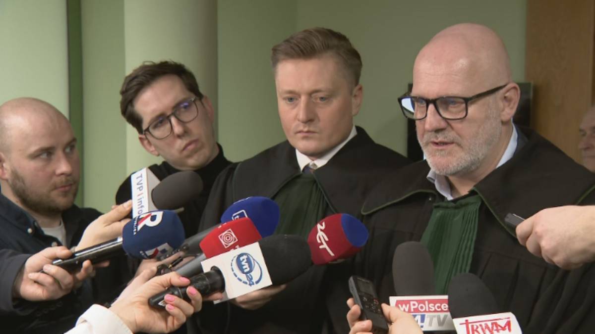 Konferencja prasowa prawnik&oacute;w otoczonych przez mikrofony medi&oacute;w.