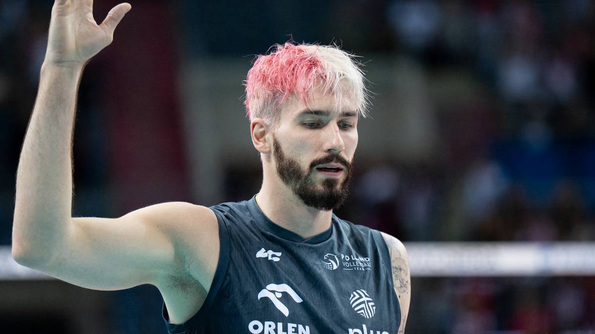 Portret siatkarza z blond włosami z r&oacute;żowymi końc&oacute;wkami, ubrany w ciemny sportowy top z logo Orlen, z uniesioną prawą ręką.