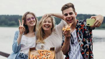 Trzy młode osoby cieszą się pizzą i robią sobie selfie.