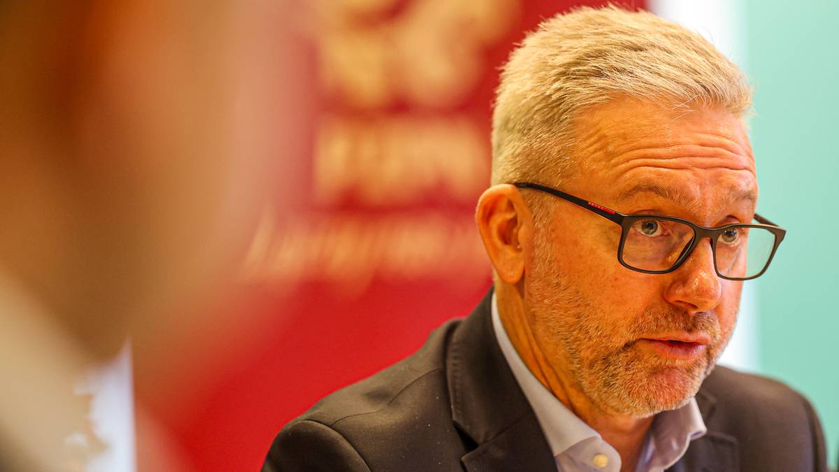 Mężczyzna w okularach, prawdopodobnie trener piłkarski, w garniturze, wypowiadający się podczas spotkania.