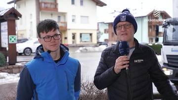 Dw&oacute;ch mężczyzn stoi na zewnątrz, jeden z nich trzyma mikrofon i m&oacute;wi. Na twarzach obu mężczyzn widać uśmiech.