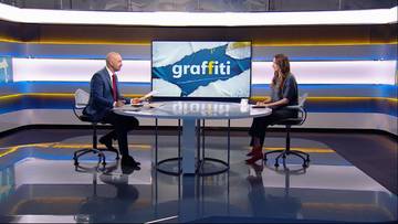 Dwie osoby siedzą przy okrągłym stole w studiu telewizyjnym. Na dużym ekranie umieszczonym za nimi wyświetla się napis "graffiti" na tle fragmentu białej ściany z niebieskimi i żółtymi elementami.