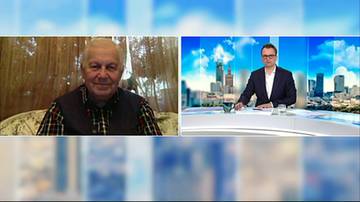 Dw&oacute;ch mężczyzn w rozmowie. Po lewej starszy mężczyzna siedzi w pomieszczeniu, po prawej młodszy mężczyzna siedzi przy stole w studiu telewizyjnym na tle panoramy miasta.