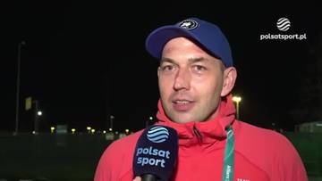 Zbigniew Br&oacute;dka, polski łyżwiarz szybki, w czapce z daszkiem, w czerwonej kurtce, udziela wywiadu. Trzyma mikrofon z logo Polsat Sport. W tle nocne oświetlenie.