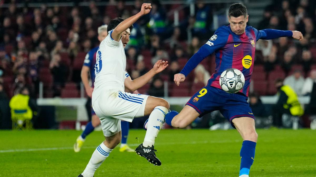 Piłkarz w niebieskiej koszulce z numerem 9 próbuje przejąć piłkę od zawodnika w białej koszulce na zielonej murawie stadionu.