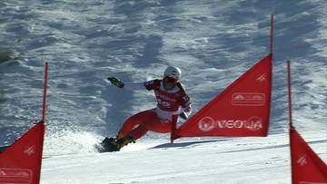 Zawodniczka na nartach w kombinezonie narciarskim zjeżdża po ośnieżonym stoku, mijając czerwone flagi wyznaczające trasę slalomu r&oacute;wnoległego.
