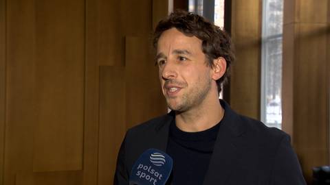 Portret Filipa Gawęckiego, mężczyzny w średnim wieku z kr&oacute;tkimi włosami i zarostem, ubranego w ciemną marynarkę i czarny golf, udzielającego wywiadu z mikrofonem Polsat Sport.