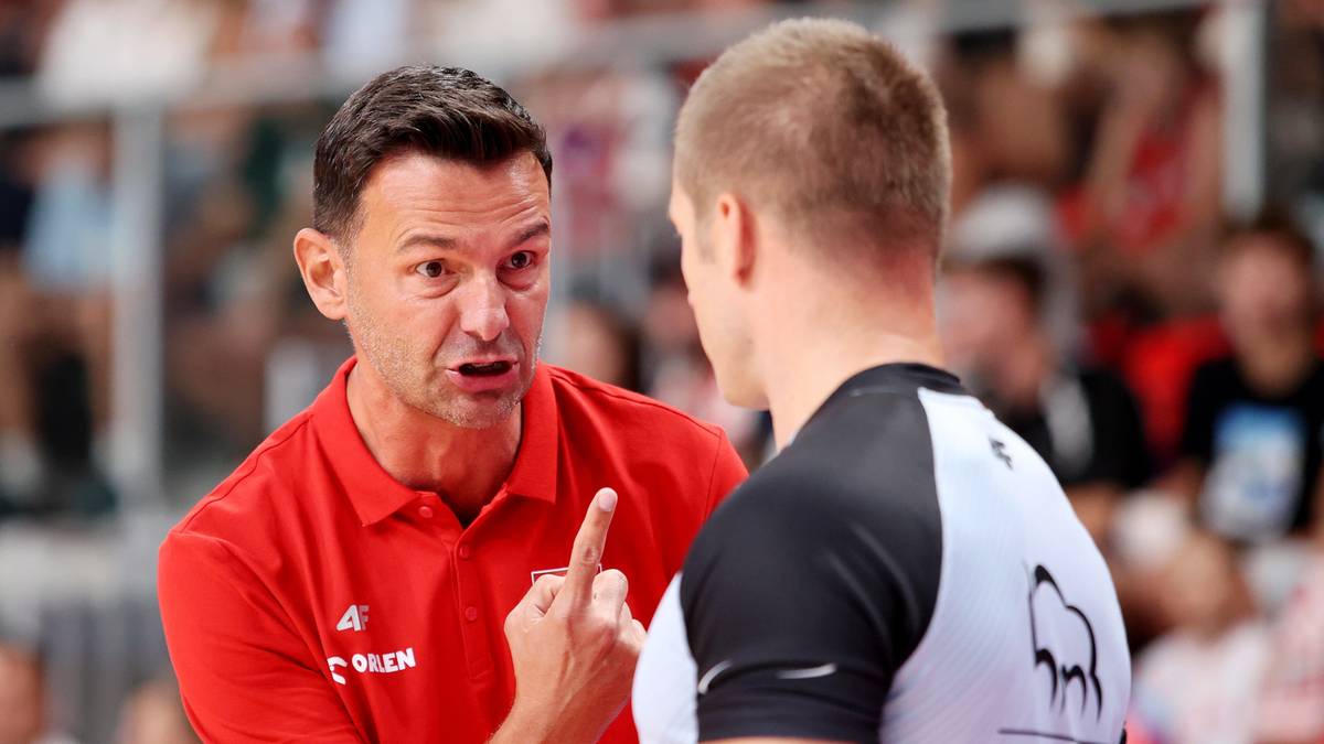 Trener w czerwonej koszulce udziela wskaz&oacute;wek zawodnikowi w białej koszulce, wskazując palcem.