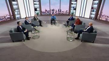 Grupa siedmiu mężczyzn w garniturach bierze udział w dyskusji w studiu telewizyjnym.