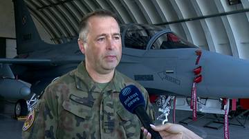 Polski pilot w mundurze wojskowym stoi przed szarym myśliwcem.