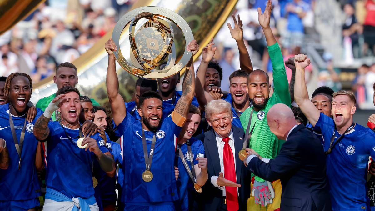Grupa piłkarzy w niebieskich strojach świętuje ze złotym trofeum, a obok nich stoi Donald Trump.