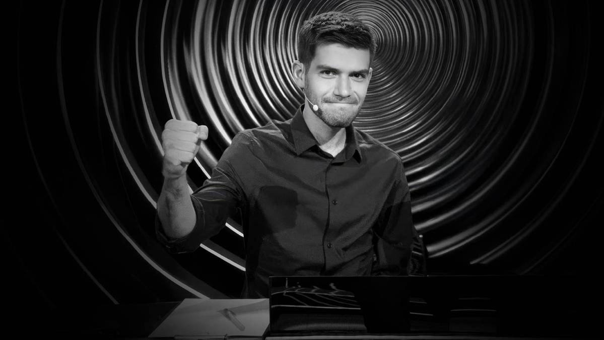 Młody mężczyzna w czarnej koszuli z zaciśniętą pięścią uniesioną do g&oacute;ry, uśmiecha się.