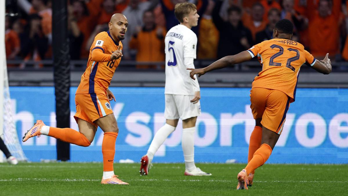 Trzech piłkarzy na boisku. Dwóch w pomarańczowych strojach, jeden w białym. Jeden z pomarańczowych zawodników biegnie w kierunku kamery, a drugi od niej się odwraca, prawdopodobnie po strzeleniu bramki. Zawodnik w białym stroju stoi pomiędzy nimi, patrząc w kierunku uciekającego gracza.