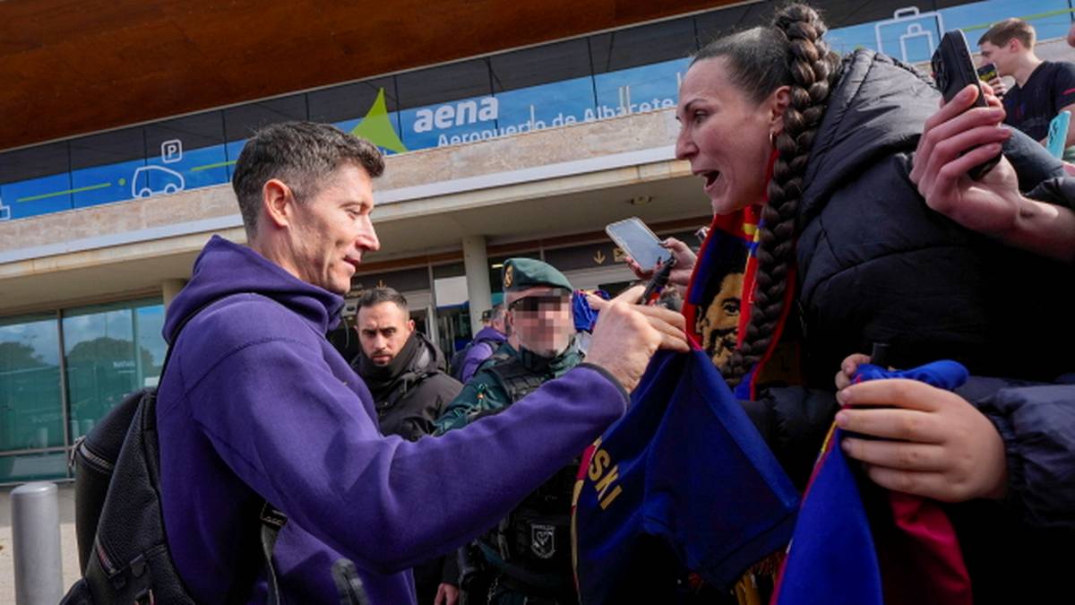 Piłkarz Robert Lewandowski w fioletowej bluzie z kapturem podaje rękę kibicowi, kt&oacute;ry trzyma koszulkę Barcelony.