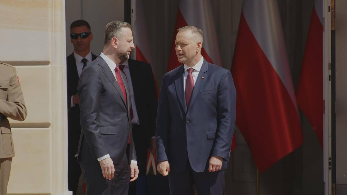 Dw&oacute;ch mężczyzn w garniturach rozmawia na tle polskich flag.