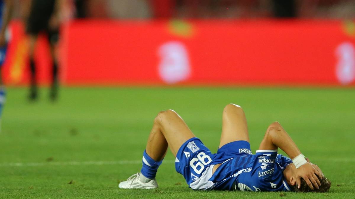 Piłkarz w niebieskim stroju Lecha Poznań leży na boisku z rękami na głowie, wyrażając zrezygnowanie.