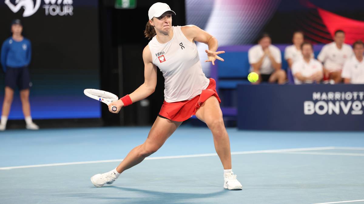 Iga Świątek wykonuje uderzenie forehandem podczas meczu tenisowego, ubrana w białą koszulkę i czerwoną spódnicę.