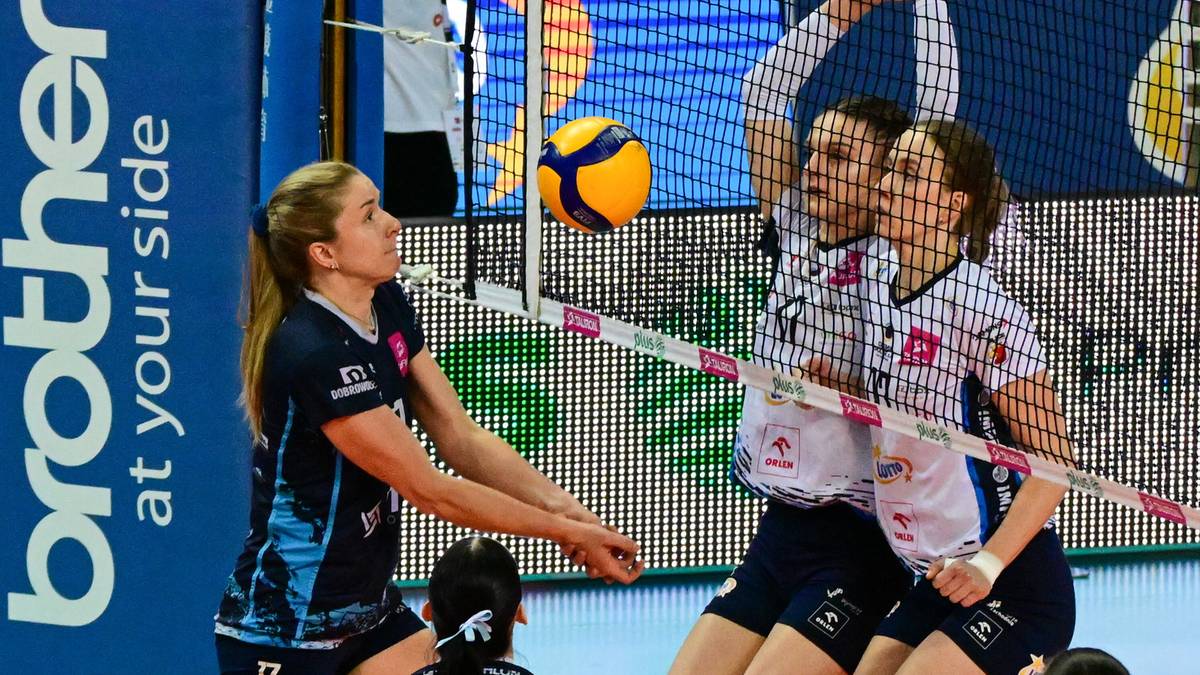 Siatkarka odbiera piłkę na boisku, siatka i inne zawodniczki w tle.