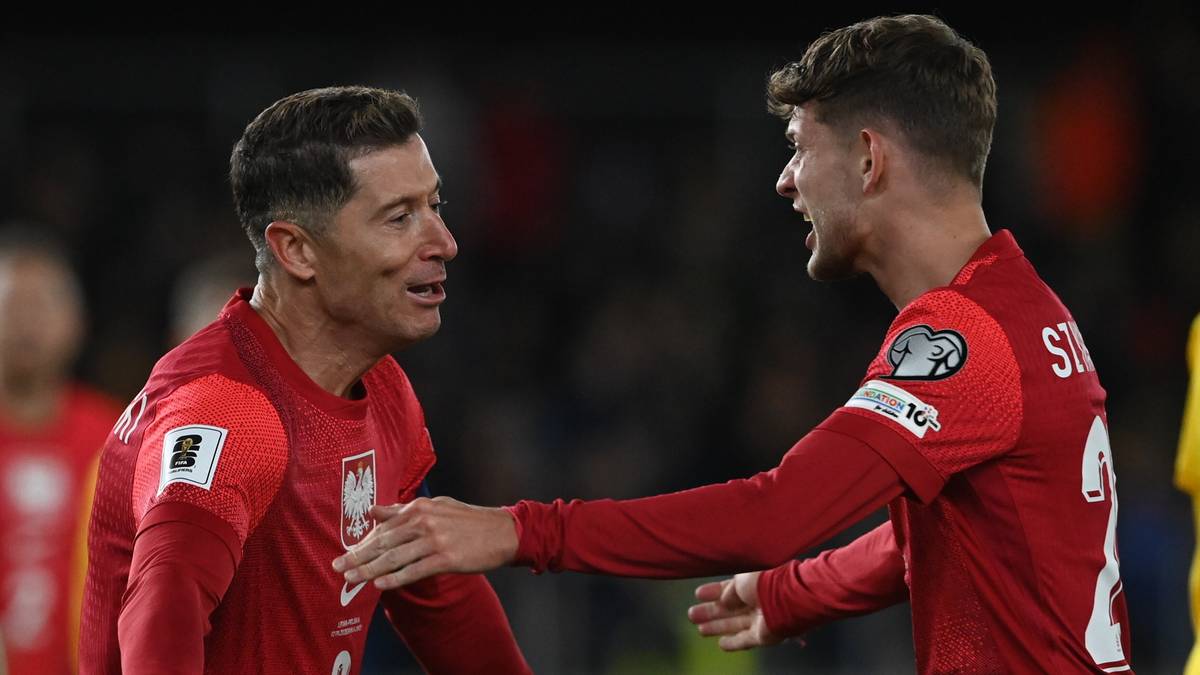 Piłkarze reprezentacji Polski w czerwonych strojach świętują bramkę, przytulając się do siebie.