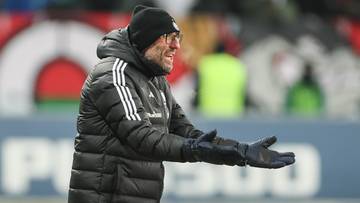 Trener Marek Papszun w czapce i kurtce zimowej, gestykuluje na boisku piłkarskim.