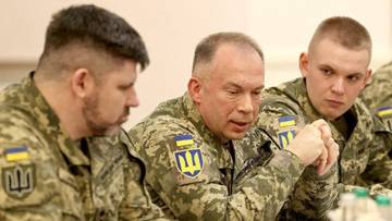 Trzech mężczyzn w mundurach wojskowych siedzi przy stole, rozmawiając.