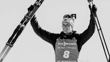 Biathlonista Sivert Bakken z nartami i kijkami w rękach, z podniesionymi ramionami.