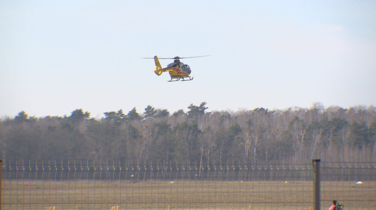 Ż&oacute;łty helikopter Lotniczego Pogotowia Ratunkowego w locie na tle nieba i drzew.