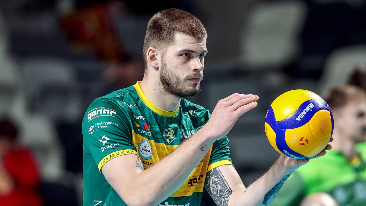 Siatkarz w zielonej koszulce trzyma piłkę do siatkówki.