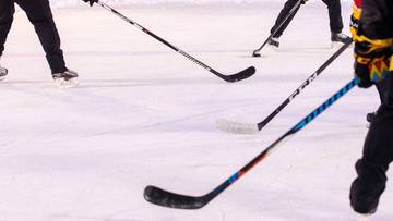 Hokeiści na lodowisku z kijami w rękach.