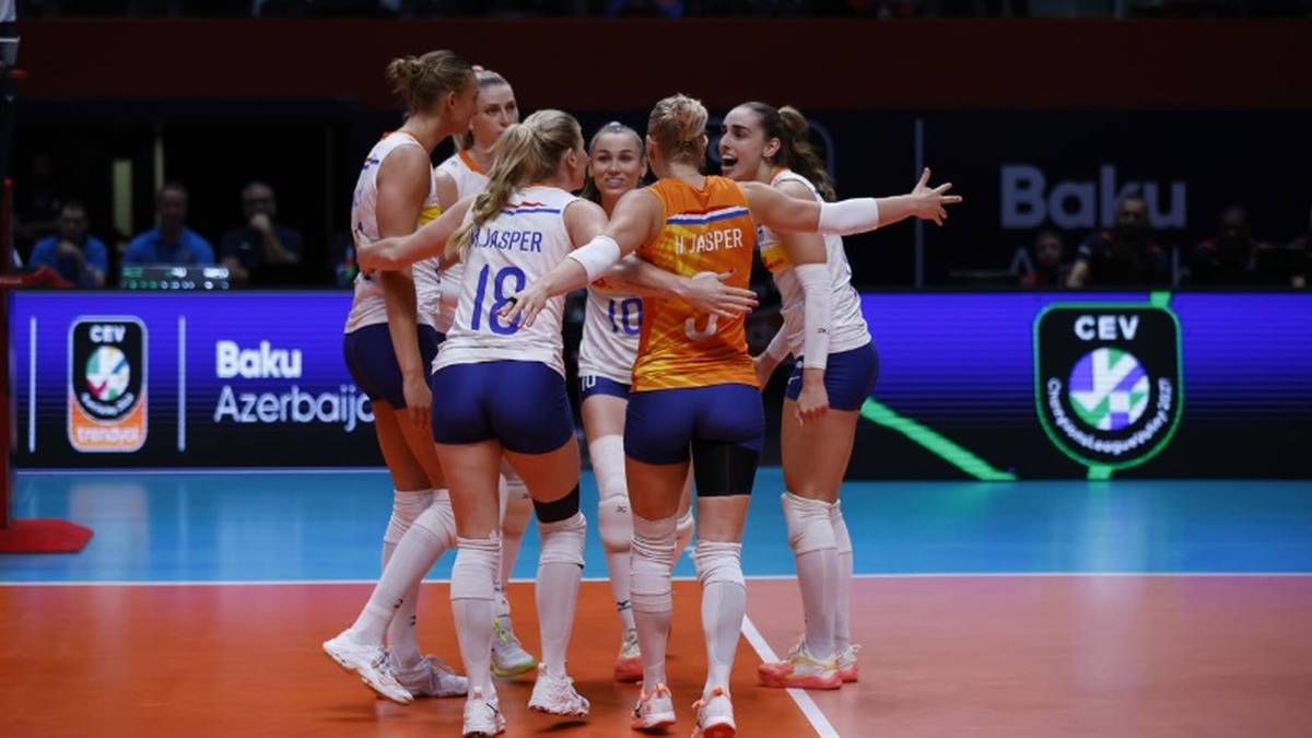 Grupa zawodniczek drużyny siatkarskiej w białych i pomarańczowych strojach sportowych przytulająca się i świętująca zwycięstwo na boisku.