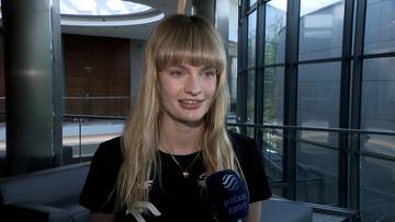 Młoda kobieta z blond włosami i grzywką, ubrana w czarną koszulkę, uśmiecha się trzymając mikrofon "Polsat Sport".