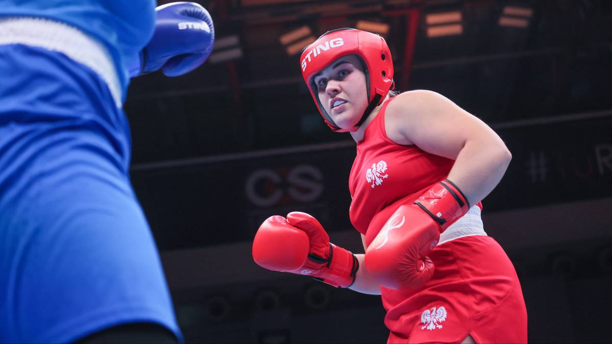 Polka w czerwonym stroju bokserskim i kasku walczy na ringu.